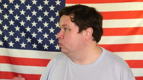 Side view of young fat man who invites someone on the background of an USA flag Stock Footage 107094777