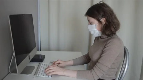 Side view of a young girl working at a computer at home in a medical mask during Stock Footage 127571759