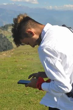 Side view of a young guy using his phone in the mountain  Stock Photos