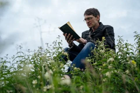Side view of young handsome man in glasses and warm jacket reading book in open Stock Photos