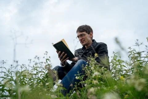 Side view of young handsome man in glasses and warm jacket reading book in open Stock Photos