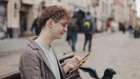 Side View of Young Hipster Guy in Glasses and Jacket Using his Smartphone Video stock 115321393