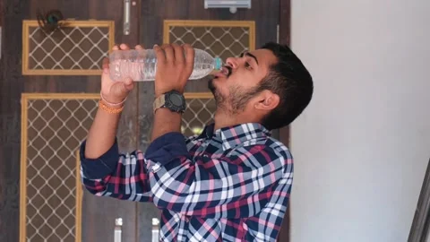 Side view of a young Indian man drinking water from a plastic bottle 스톡 동영상 329922040