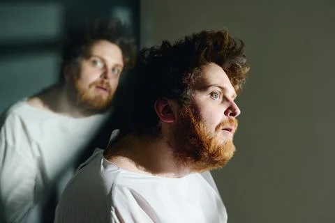 Side view of young insane man in white straitshirt sitting in front of camera Stock Photos