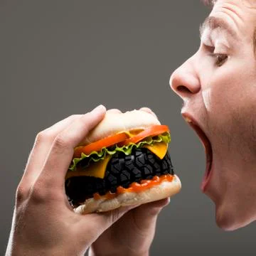 Side view of young man about to bite a tire hamburger, close up Stock Photos