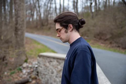 Side view of young man alone outdoors looking down in contemplation Stock Photos