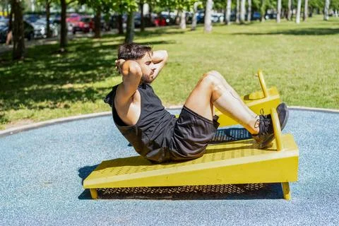 Side view of a young man doing sit-ups on outdoor fitness equipment Stock Photos