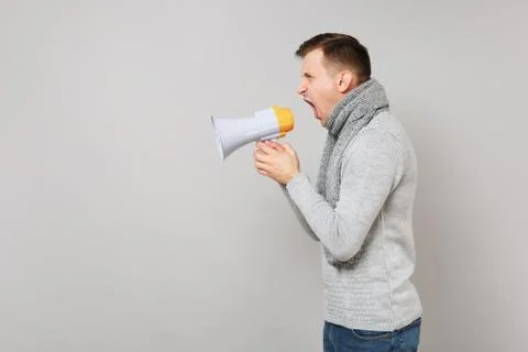 Side view of young man in gray sweater, scarf scream in megaphone isolated on Stock Photos