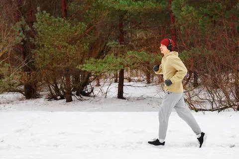 Side view of a young man jogging in a snowy forest. Male runner in headphon.. Stock-Fotos