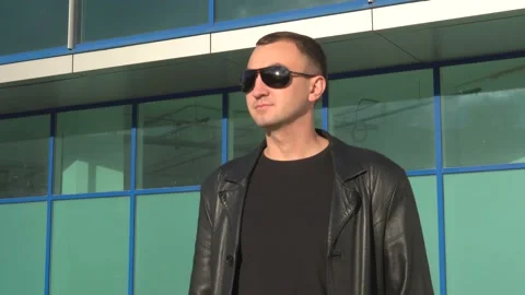 Side view of young man in leather jacket and sunglasses standing outdoor Stock Footage 97883285