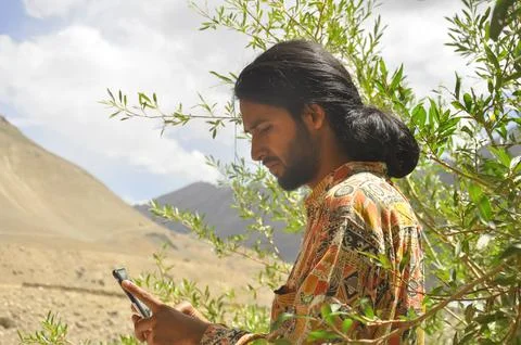 Side view of a young man with long hair and beard using phone Stock Photos