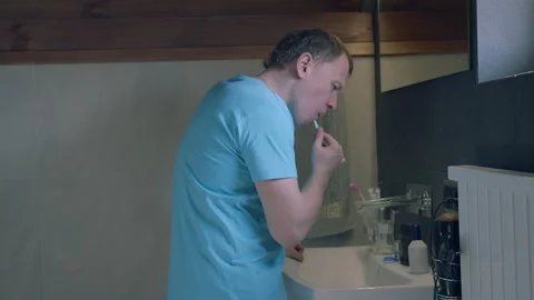 Side view of young man looking in mirror, brushing teeth, camera tracking Stock Footage 154563432