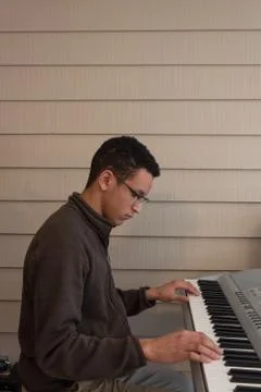 Side view of a young man playing an electric keyboard, hands wide apart Stock Photos