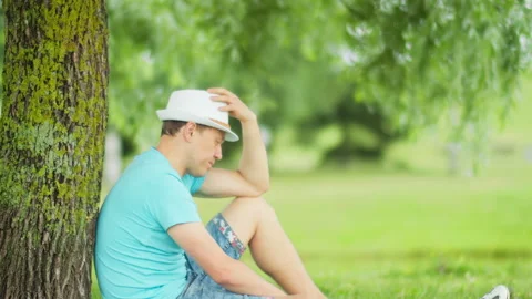 Side view of a young man sitting under a tree in the park Stock Footage 149240287