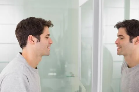 Side view of a young man smiling at self in bathroom mirror Stock Photos