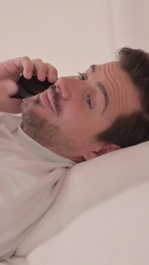 Side View of Young Man Talking on Phone in Bed, vertical video 库存影片 328565126