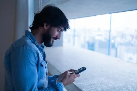 Side view of young man using a smartphone with city view landscape in the bac Stock Photos