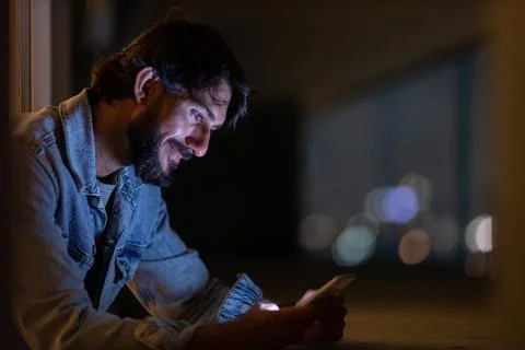 Side view of young man using a smartphone at night time with city view landsc Stock Photos