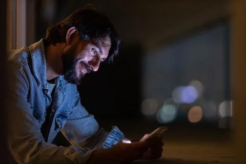 Side view of young man using a smartphone at night time with city view landsc Stock Photos