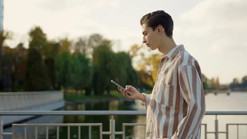 Side View of the Young Man Walking oin the Park Using his Smartphone, Chatting Stock Footage 237462000