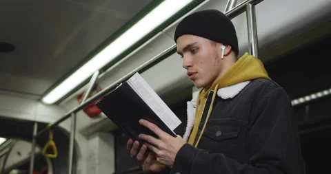 Side view of young man with wireless earpods turning pages while enjoing story 動画素材 136291338