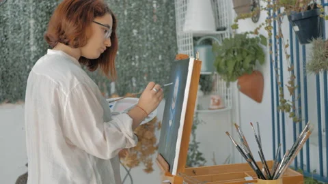 Side view young painter with blouse on outdoor patio painting a picture 스톡 동영상 130617654