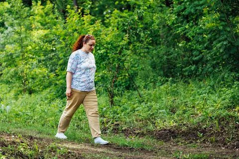 Side view of young plump buxom woman with long curly red hair walking on path in Stock Photos