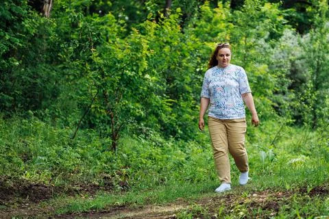 Side view of young plump buxom woman with long curly red hair walking on path in Stock Photos