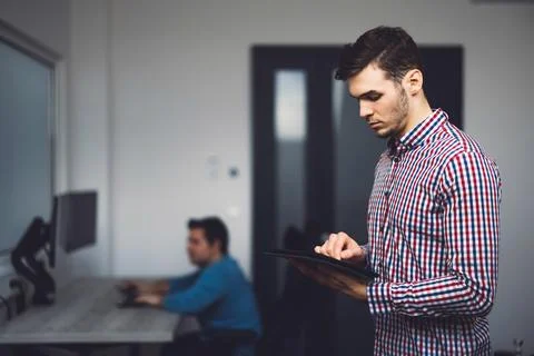 Side view of young programmer standing in the office looking down at the digital Stock Photos