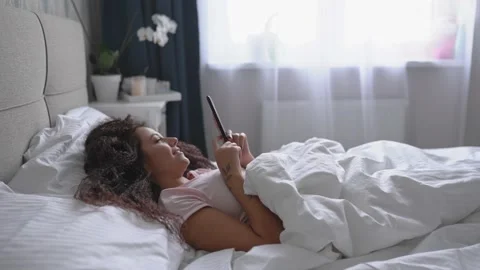 Side view of young smiling woman lie on the bed and use smartphone. Social media Stock Footage 142824910