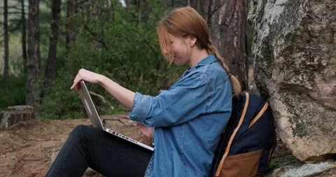Side view young woman backpacker in forest with laptop sitting by a rock. Stock Footage 151858865