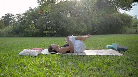 Side View of Young Woman Practicing Yoga Laying on a Mat in a Park Under a tree Stock Footage 194905663
