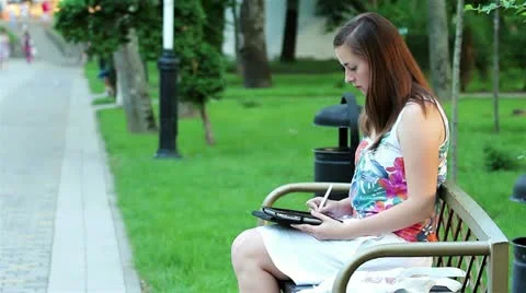 Side view of a young woman using a tablet computer on a park bench.  Video stock 21313815