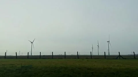 Side Window Shot of Wind Turbines Farm on Green Fields Under Overcast Sky in Stock Footage 337043681
