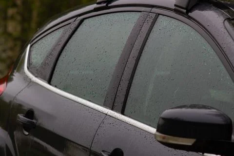Side windows of a dark-colored car covered in raindrops. Фото