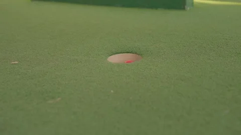 Sideview close up slow motion mini golf ball hits hole in one Stock Footage 272805714