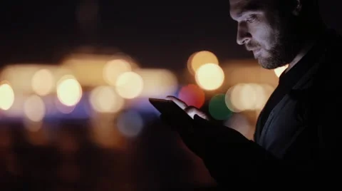 Sideview of a handsome man, smiling, nodding, using his tablet at night. Blurred Stock Footage 67950105