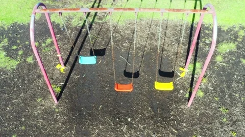 Sideview of three swings in red, yellow and blue coloration, still swinging Stock Footage 146342794