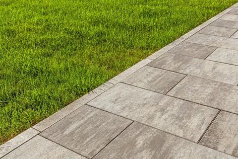 The sidewalk paved with large slabs is separated from the mowed lawn by a cur Foto stock