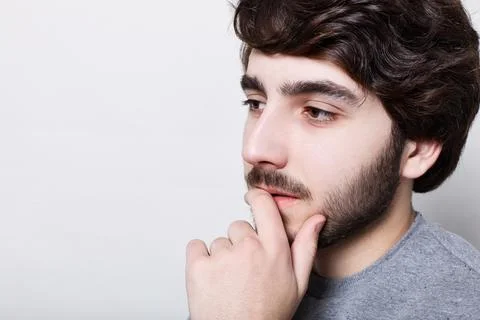 A sideways close-up of bearded thoughtful man with stylish haircut holding hi Stock Photos