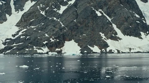 Sideways Pan Along Jagged Snow-Patched Antarctic Rocky Coastline and Dark Icy 動画素材 334093144