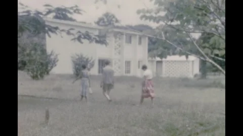 Sierra Leone 1950s, View of three people walking through a garden beside house Stock Footage 299736241
