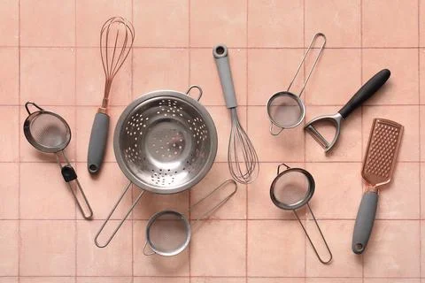 Sieves with colander and different kitchen utensils on pink tile background Stock Photos