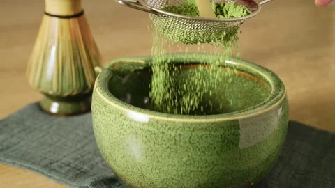 Sifting bright green matcha powder using metal mesh sieve over ceramic bowl Stock Footage 345166291