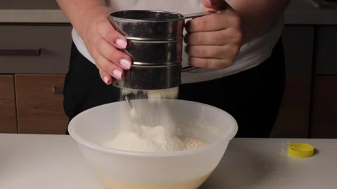 Sifting flour into mixing bowl using metal sifter. close-up of ingredient Stock Footage 316473677
