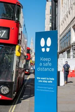A sign asking people to keep a safe distance with a bus passing by on a stree Stock Photos
