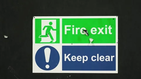Sign combining fire exit and keep clear warnings mounted on dark wall. Board Stock Footage 314825082