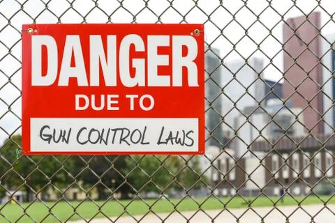 Sign danger due to gun control laws hanging on the fence Stock Photos