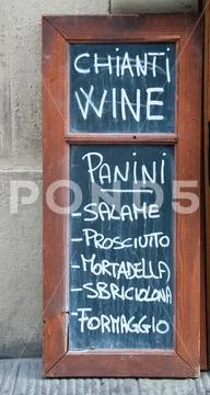 A sign indicating the sale of sandwiches, wine, ham, cheese, and mortadella Stock Photos