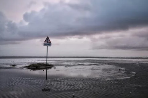 Sign on a metal pole put on the beach under a cloudy sky Stock Photos